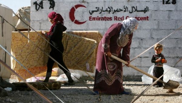 Syrian-Kurdish refugees work near tents erected by the United Arab Emirate's Red Crescent as aid is distributed at the Qushtapa refugee camp, 15 kilometers South of Arbil. [AFP]