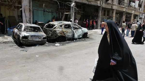An Iraqi woman walks past burnt out vehicles and damaged buildings following a car bomb explosion in Baghdad. AFP Photo