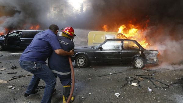 A firefighter is helped as he extinguishes fire at the site of an explosion in Beirut's southern suburb neighbourhood of Bir al-Abed on July 9, 2013. (Source: AFP/STR)
