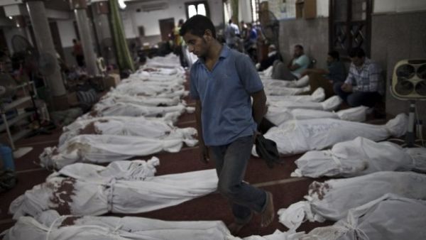 An Egyptian man walks between lines of bodies wrapped in shrouds at a makeshift morgue in Cairo on August 15, 2013, following a crackdown on the protest camps of supporters of Mohamed Morsi. (AFP)