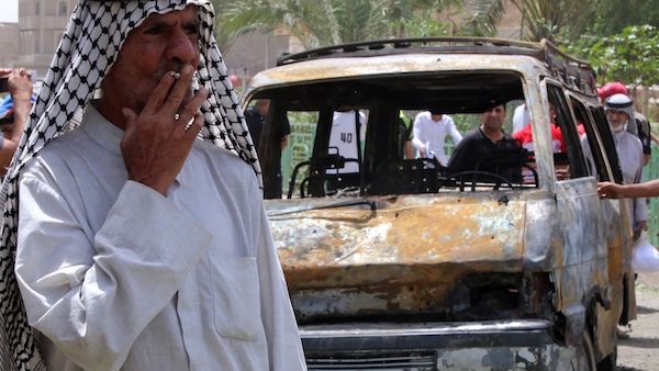 An Iraqi man smokes a cigarette in front of a burnt vehicle at the site of a car bombing at a market in Baghdad's impoverished district of Sadr City. AFP Photo