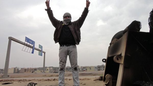 A man shows off the V-sign for victory as he stands on top of a burn out lorry on the side of the main highway leading west out of the capital Baghdad to Fallujah, on January 5, 2014. (AFP)
