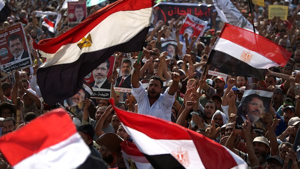 Egyptian supporters of deposed president Mohamed Morsi (portrait) wave their national flag as they attend a rally in support of the former Islamist leader outside Cairo's Rabaa al-Adawiya mosque on July 8, 2013. (Source: AFP/ MAHMUD HAMS)