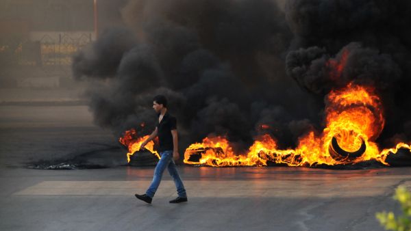 LEBANON, Tripoli : A youth walks past burning tires across a street in the northern city of Tripoli, on June 23, 2013, during protests in support of Sunni Muslim Sheikh Ahmad al-Assir whose supporters have clashed with the Lebanese army in the southern Lebanese city of Sidon. (Credit: AFP)
