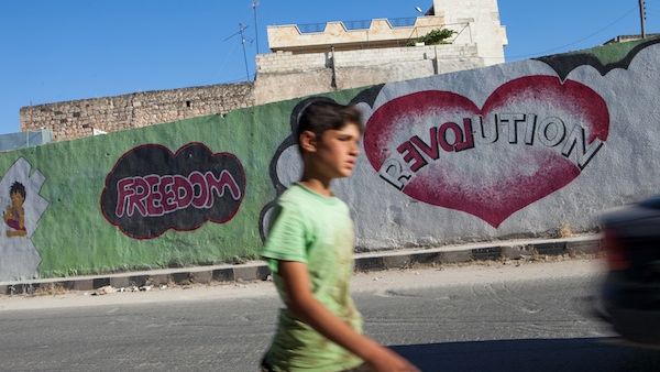  A Syrian boy walks past graffiti in the village of Kfar Nubul in the northwestern province of Idlib on Monday. (AFP)