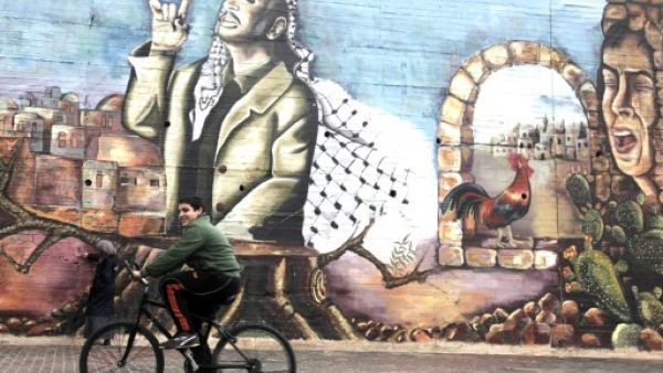 A Palestinian boy cycles past a mural painted by university students depicting the late Palestinian leader Yasser Arafat in the West Bank city of Nablus on November 9, 2013. (AFP) A Palestinian boy cycles past a mural painted by university students depicting the late Palestinian leader Yasser Arafat in the West Bank city of Nablus on November 9, 2013. (AFP)