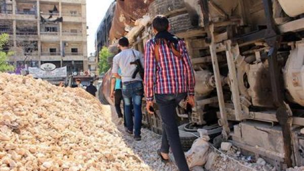 مقاتلون من الجيش السوري الحر يحملون أسلحة وهم يمرون وسط حواجز للحماية من قناصة قوات الأسد في حي سيف الدولة بحلب