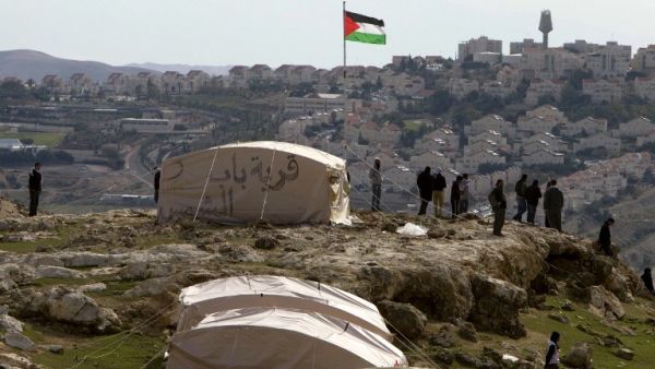 A Palestinian flag flutters as Palestinians, together with Israeli and foreign activists, stand near tents at the Bab al-Shams (Gate of the Sun) 'outpost' in the sensitive West Bank corridor east of Jerusalem on Saturday (Photo: AFP /AHMAD GHARABLI)