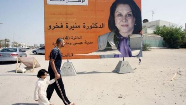 بحريني يسير مع ابنه امام ملصق انتخابي لمرشحة في البحرين
