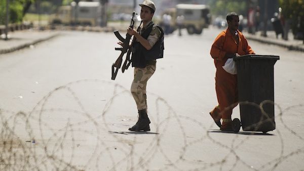 An Egyptian army soldier holds his rifle as he walks by a street cleaner behind a barbed wire checkpoint on a street in Cairo on August 23, 2013. (AFP)
