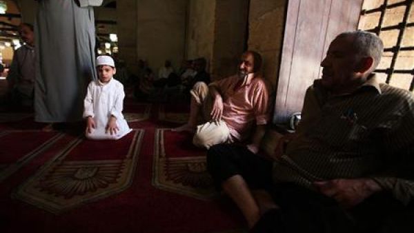 طفل يؤدي مع والده صلاة الجمعة مع والده في الجامع الازهر بالقاهرة
