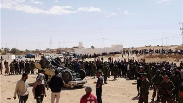 جنود من الجيش التونسي وسكان ولاجئين ليبيين بالقرب من سيارة مقلوبة تابعة للقوات القذافي بالقرب من الذهيبة 
