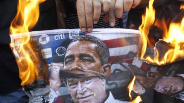 A protester holds a poster burning on which is depicted former US president George W. Bush taking off a mask of current President Barack Obama during a demonstration of in Beirut. (AFP)

