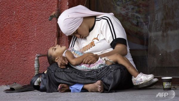 A Syrian refugee holds her child as they doze off at a street in the southern Lebanese city of Sidon. (AFP)