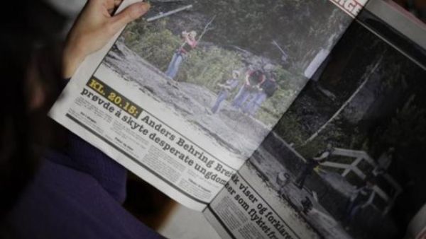 سيدة تقرأ صحيفة عليها صور لاعادة تمثيل الجريمة في جزيرة يوتويا الاحد  
