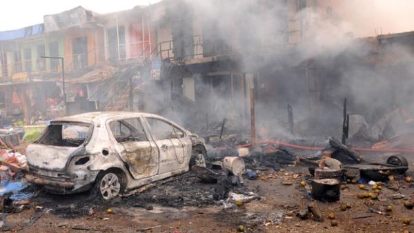 The wreckage of a burnt vehicle remains in front of burning shops following a bomb blast in central Nigeria (AFP/File)