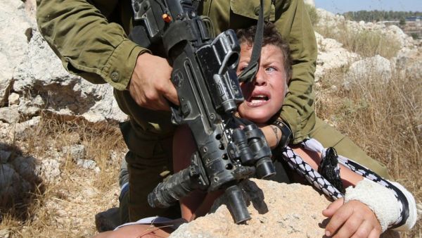 An Israeli soldier forcefully holds down eleven-year-old Mohammed Tamimi, his left arm in a cast, during clashes in the West Bank village of Nabi Saleh, August 28, 2015. (AFP/Abbas Momani)