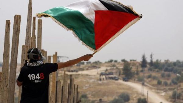 A Palestinian protester waves a Palestinian flag in front of Israeli security forces on May 13, 2016 in the West Bank village of Bilin, near Ramallah. (AFP/Abbas Momani)