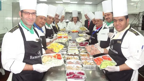 سها الترجمان مع فريق عمل المطبخ اثناء تحضير الوجبات المغلفه لبنك الطعام المصري.