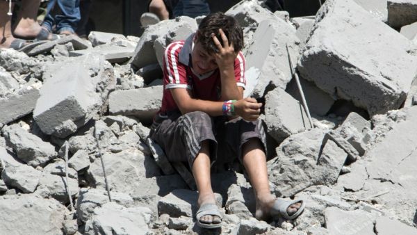 A young Syrian boy cries as he sits on the rubble after a missile fired by Syrian government forces hit a residential area in the northern Syrian city of Aleppo on July 21, 2015. (AFP/Karam al-Masri)