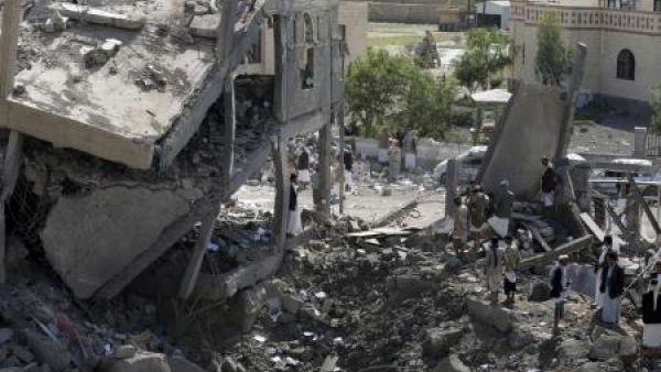 متشددون حوثيون يقفون على أنقاض مبنى دمر في غارة جوية بمدينة عمران
