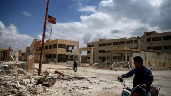 مواطن على دراجته وآخر يمر أمام مبنى مدمر في منطقة خاضعة لسيطرة المعارضة في الغوطة الشرقية بسوريا
