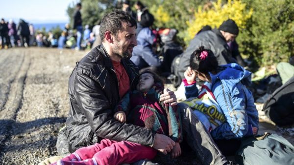 A man sits holding a child on the side of a road after being detained by Turkish soldiers with other Syrians trying to reach the Greek island of Lesbos from Dikili, western Turkey, on March 5, 2016. (AFP/Bulent Kilic)
