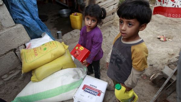 Yemeni children stand next to food rations that a local charity is distributing to families affected by the country's ongoing conflict during the fasting month of Ramadan on June 15, 2016 in an empoverished part of the capital Sanaa. (AFP/Mohammed Huwais)