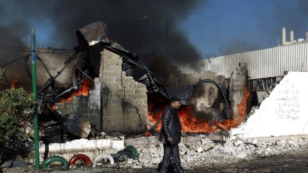A Yemeni man walks past flames rising from the ruins of buildings destroyed in an air-strike by the Saudi-led coalition on February 10, 2016 in the capital Sanaa. (AFP/Mohammed Huwais)
