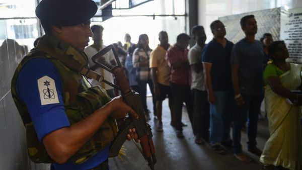 A Sri Lankan Navy personnel stands guard as Catholic devotees pray at St. Anthony's church after it was partially opened for the first time since the Easter Sunday attacks in Colombo (AFP)