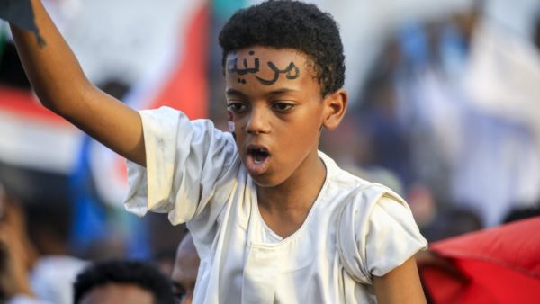 A Sudanese boy wearing facepaint on his forehead reading in Arabic "civilian" chants slogans while seated on the shoulders of a man as people celebrate after protest leaders struck a deal with the ruling generals on a new governing body, in the capital Khartoum's eastern district of Burri (AFP)
