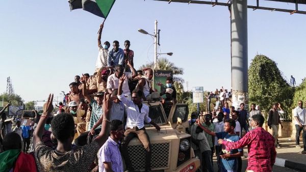 Sudanese protesters wave a national flag and flash the victory sign as they sit atop a military vehicle next to soldiers near the capital Khartoum's military headquarters on April 7, 2019. (AFP)