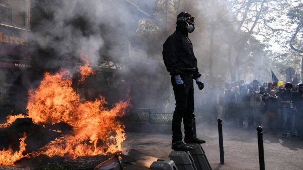 A masked protester dressed in black stands next to a burning barricade during clashes on the sidelines of a May Day demonstration in Paris, on May 1, 2019. (Anne-Christine POUJOULAT / AFP)
