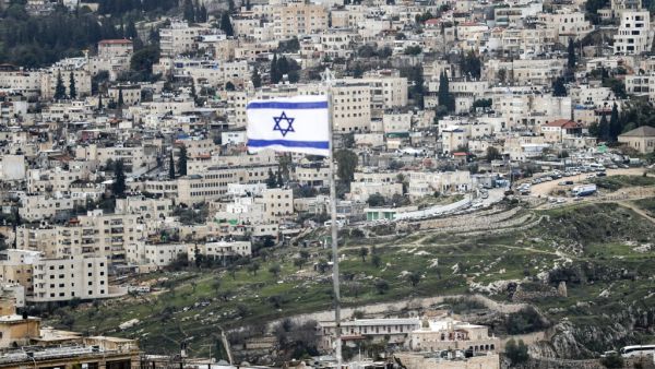 This picture taken on January 24, 2020 from the Mount of the Olives shows an Israeli flag flying (foreground) with the Jerusalem neighbourhood of Abu Tor seen in the background. AHMAD GHARABLI / AFP