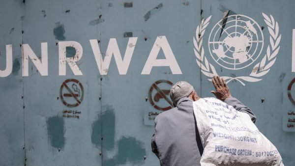 A Palestinian man stands in front of the emblem of the UN Relief and Works Agency for Palestine Refugees in the Near East (UNRWA) outside the agency's offices in Gaza City, July 31, 2018. (AFP/ File Photo)
