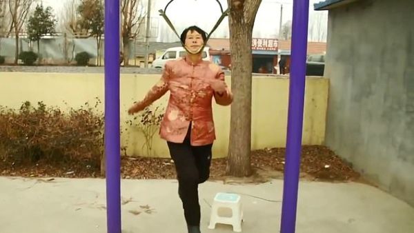 Pensioner Song Lianyun, 68, carefully placing her head between two straps, one of them under her jaw and one of them at the nape of her neck. (Pear Video Screenshot)