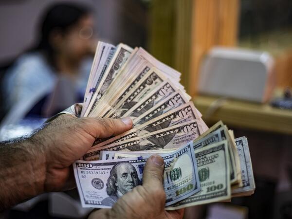 A merchant holds a wad of Syrian pounds (L) and US dollars at a market in the Kurdish-majority city of Qamishli in northeast Syria.  Delil SOULEIMAN / AFP