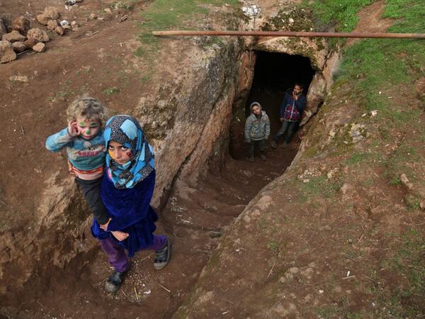 Children walk through the entrance of an underground shelter where several families of internally displaced Syrians from Aleppo and Idlib provinces are taking refuge, in the village of Taltunah about 15 kilometres northwest of Idlib in the northwestern Idlib province, on February 23, 2020. Aref TAMMAWI / AFP
