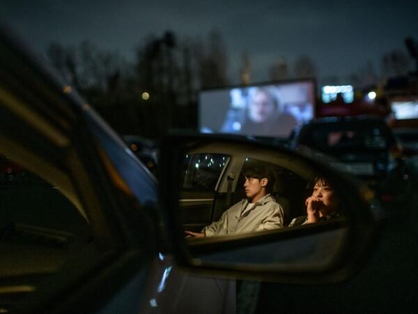 In a photo taken on March 21, 2020 a couple sit in their car as they watch a movie screening at a drive-through cinema in Seoul. Box office numbers in South Korea -- which has 8,897 confirmed virus cases -- have plummeted in recent weeks due to the epidemic, with authorities urging the public to avoid large crowds. But at drive-in cinemas, moviegoers can enjoy a movie from the comfort of their cars, parked in front of a large outdoor screen.  Ed JONES / AFP