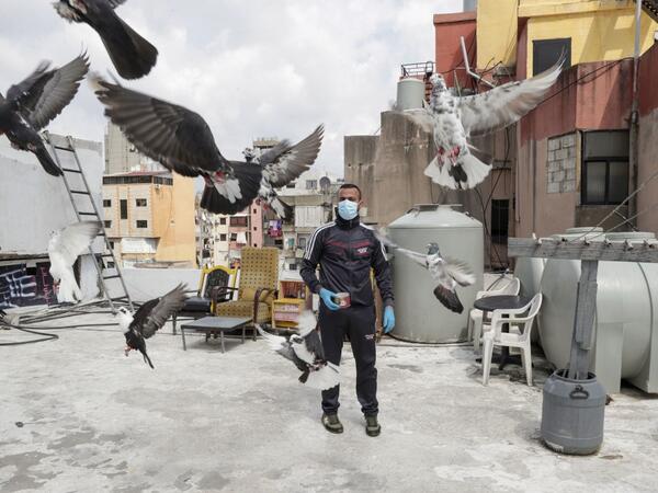 A pigeon owner, wearing personal protective equipment, watches his pigeons fly on the rooftop of his building in the southern suburb of Beirut on April 11, 2020. ANWAR AMRO / AFP