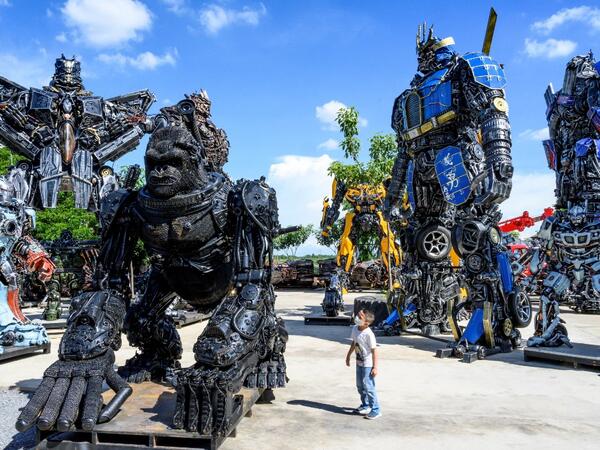 This photograph taken on July 18, 2020 shows a child looking at a figure of King Kong in front of life-sized sculptures of characters from the "Transformers" film franchise, all made of scrap metal parts, at the Ban Hun Lek museum in Ang Thong, some 100km north of Bangkok. "Ban Hun Lek" or "The House of Steel Robots" is a museum where a collective of artists display their scrap metal creations depicting popular comics and sci-fi film characters. Mladen ANTONOV / AFP