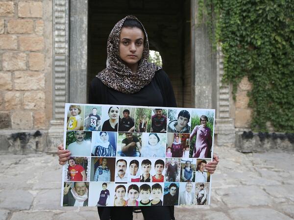 Yazidi woman Ashwaq Haji, allegedly used by the Islamic State group (IS) as a sex slave, holds portraits of jihadists' victims from her village of Kocho near Sinjar, as she visits the Lalish temple, in Lalish, northern Iraq, on August 15, 2018. - A young Yazidi woman who fled to Germany but returned home to northern Iraq says she cannot escape her Islamic State group captor who held her as a sex slave for three months. Ashwaq Haji, 19, says she ran into the man in a German supermarket in February. Traumatis