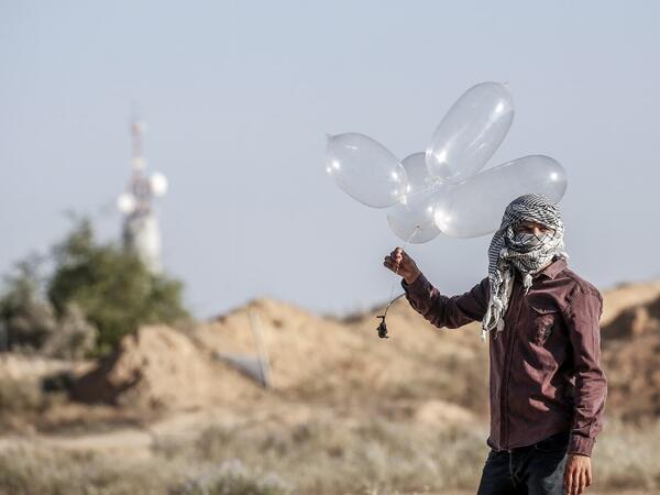 A Palestinian prepares to launch inflated condoms attached with an incendiary device to be directed and flown towards Israel, near Rafah along the border between the Gaza Strip and Israel on August 21, 2020. SAID KHATIB / AFP