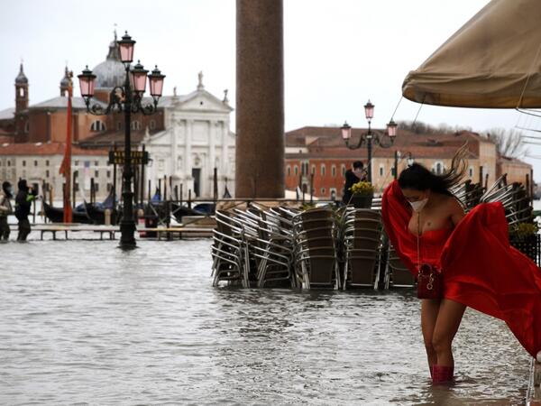 A view shows a model holding her dress on a flooded St. Mark's Square on December 8, 2020 following a high tide "Alta Acqua" event following heavy rains and strong winds, and the mobile gates of the MOSE Experimental Electromechanical Module that protects the city of Venice from floods, were not lifted. ANDREA PATTARO / AFP