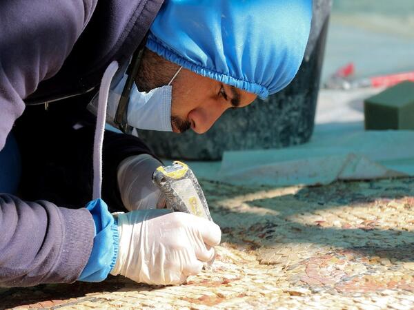 A worker employed by a pilot project run by the UN cultural agency UNESCO, restores a mosaic floor at an ancient church complex, in the small town of Rihab, some 70 kilometres north of the Jordanian capital Amman, on February 9, 2021. In the ruins of the ancient Byzantine church in Jordan, local townspeople and Syrian refugees work side by side on a project that unites preserving cultural heritage and fighting poverty.  Khalil MAZRAAWI / afp