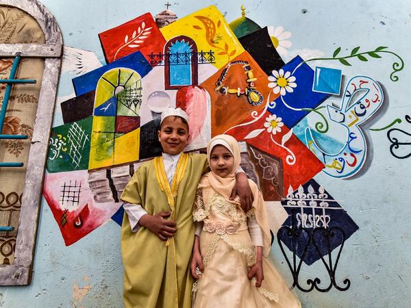 Children pose for a photo in front of a large graffiti depicting cultural elements including mosques
