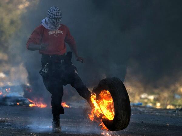 A Palestinian protestor kicks a burning tire towards Israeli security forces during clashes in the West Bank city of Nablus, following a demonstration against US President Donald Trump's decision to recognize Jerusalem as the capital of Israel on Dec. 9, 2017. 
(JAAFAR ASHTIYEH / AFP)