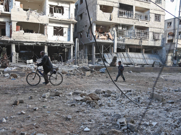 Syrian civilians walk past destroyed buildings following government bombing in the rebel-held town of Hamouria, in the besieged Eastern Ghouta region on the outskirts of the capital Damascus, on February 19, 2018. Heavy Syrian bombardment killed 44 civilians in rebel-held Eastern Ghouta, as regime forces appeared to prepare for an imminent ground assault. (ABDULMONAM EASSA / AFP)