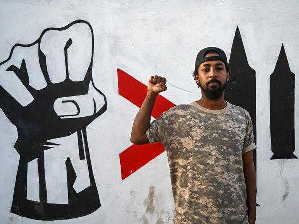 Sudanese graffiti artist Amir Saleh poses in front of a recently painted mural made by his team during a protest near the army headquarters in the capital Khartoum (AFP)