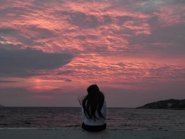 A young migrant girl watches the sunset at the city of Vathy on the island of Samos early.   LOUISA GOULIAMAKI / AFP